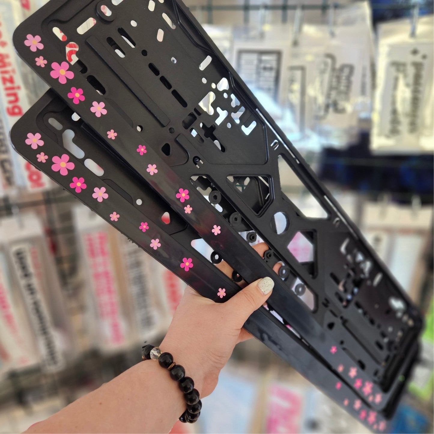Black phone case with pink floral patterns held by a hand in a store setting