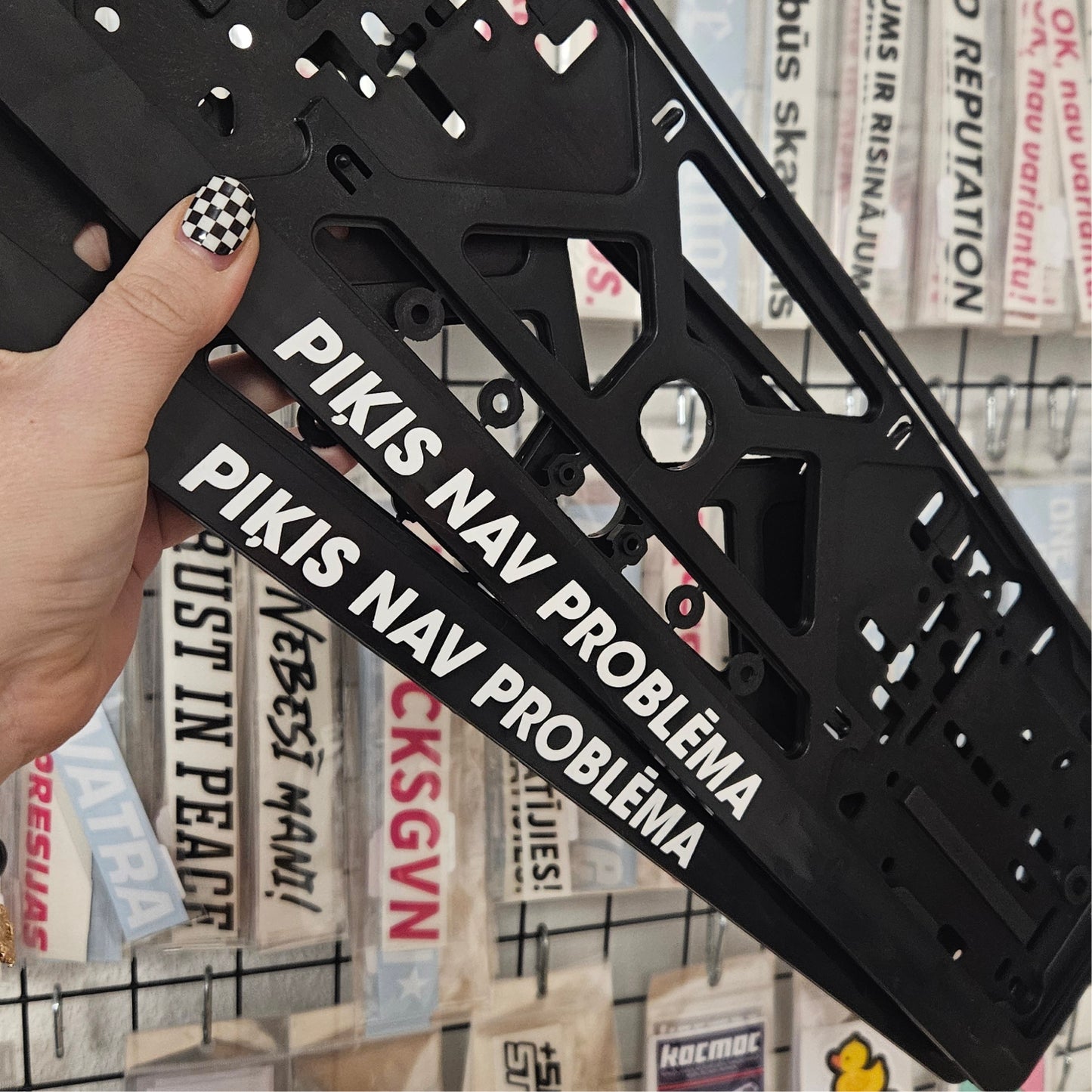 Black metal bracket with text held by a hand against a background of various posters.