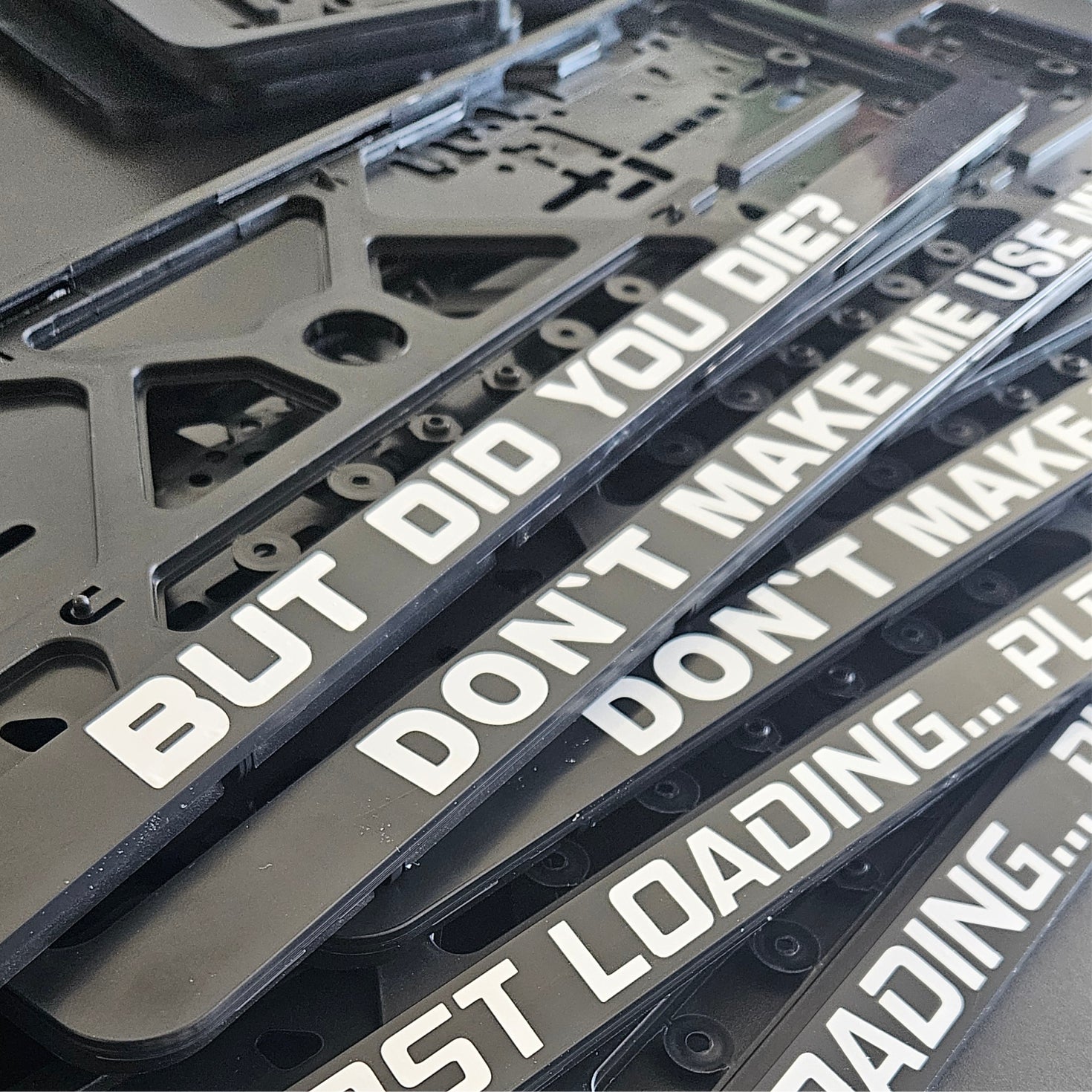 Stack of license plate frames with humorous text on a gray background