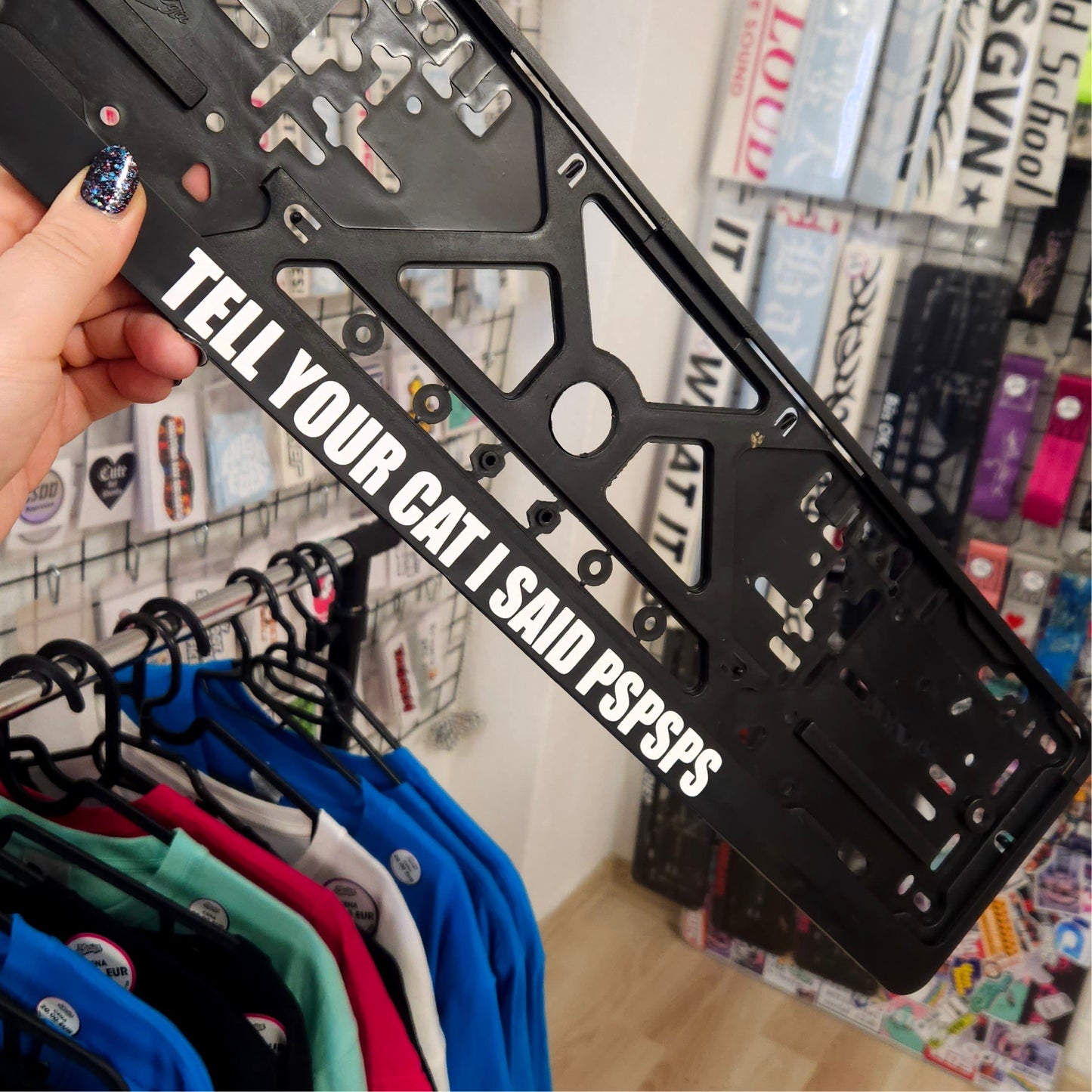 Person holding a black license plate frame with text in a store setting