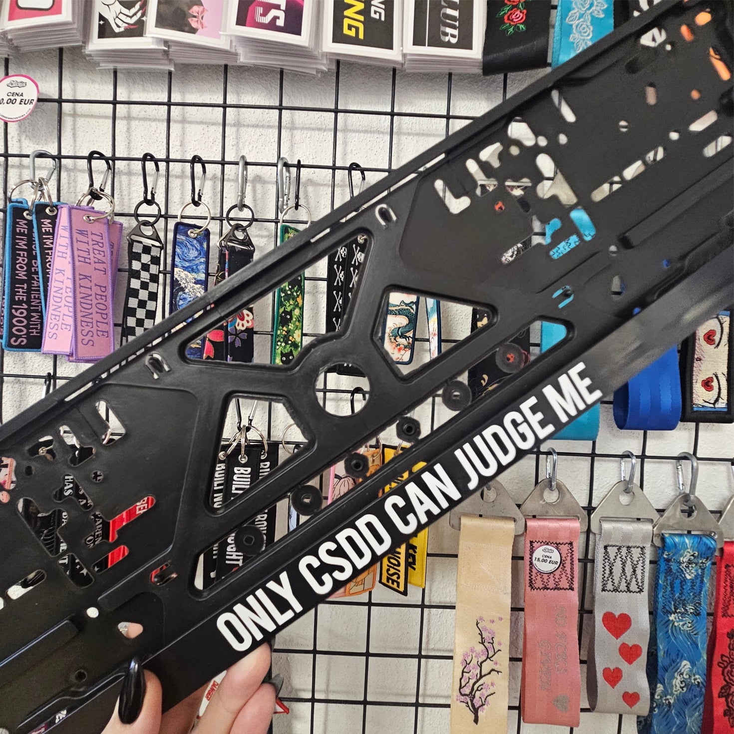 Black crossbow stock with 'Only CSDD Can Judge Me' text held in front of a wall of colorful keychains.