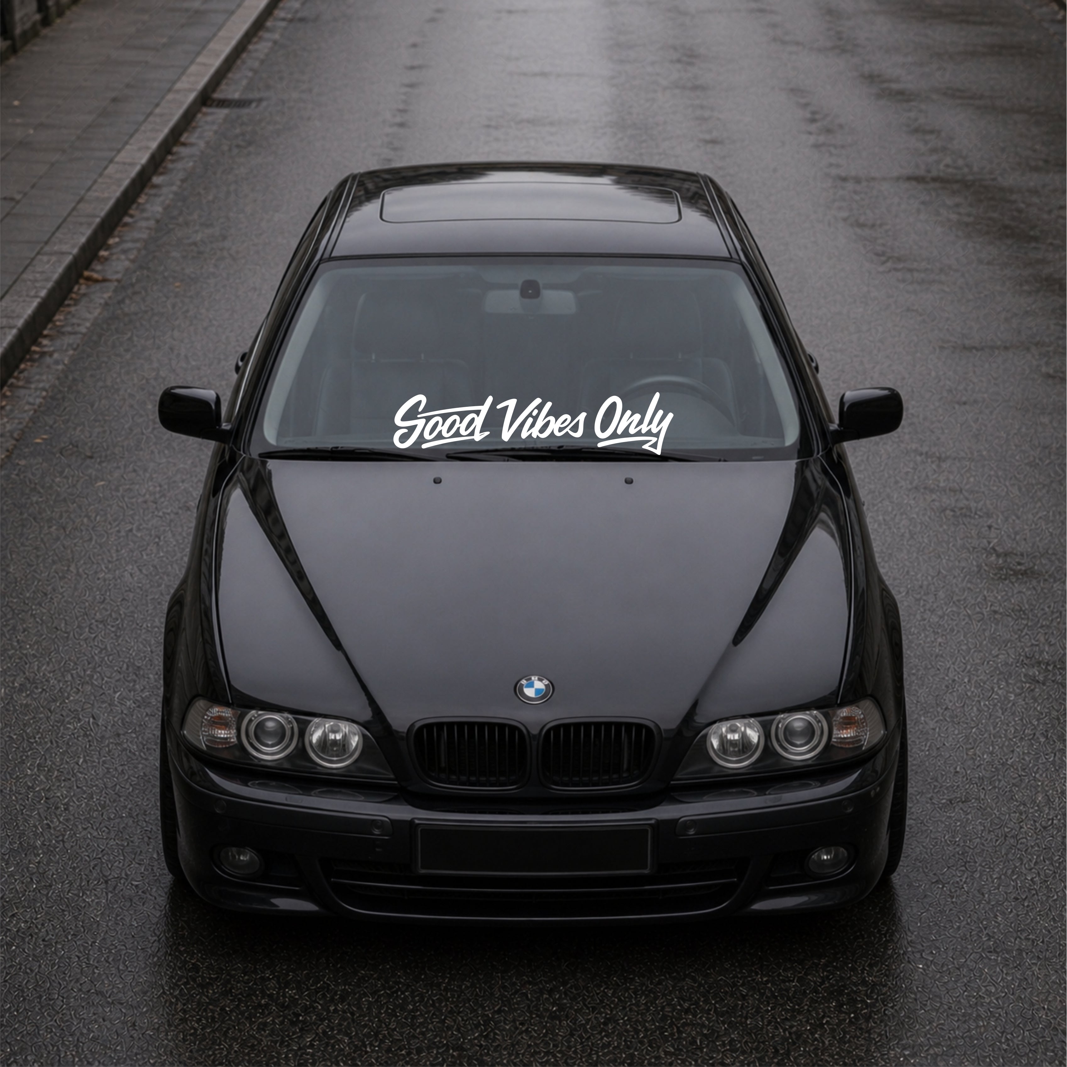 Black BMW car on a road with 'Good Vibes Only' decal on the windshield.