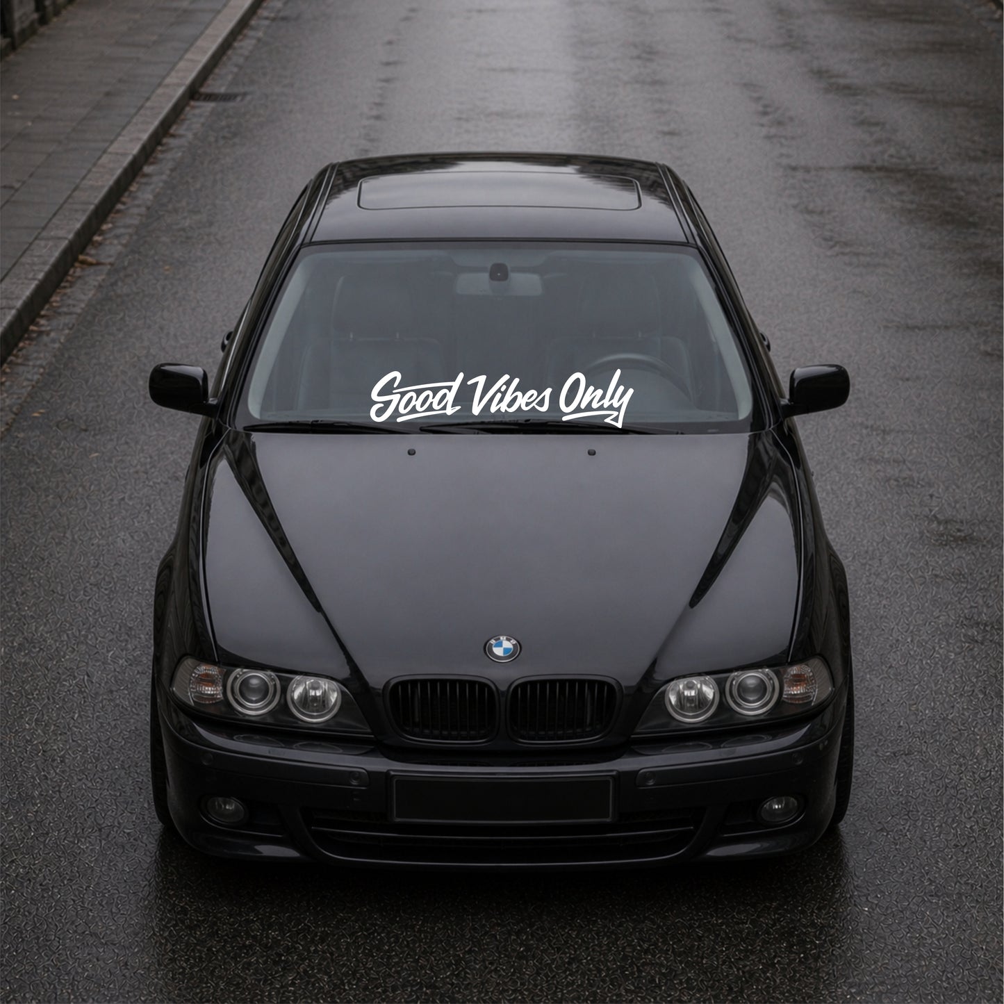 Black BMW car on a road with 'Good Vibes Only' decal on the windshield.
