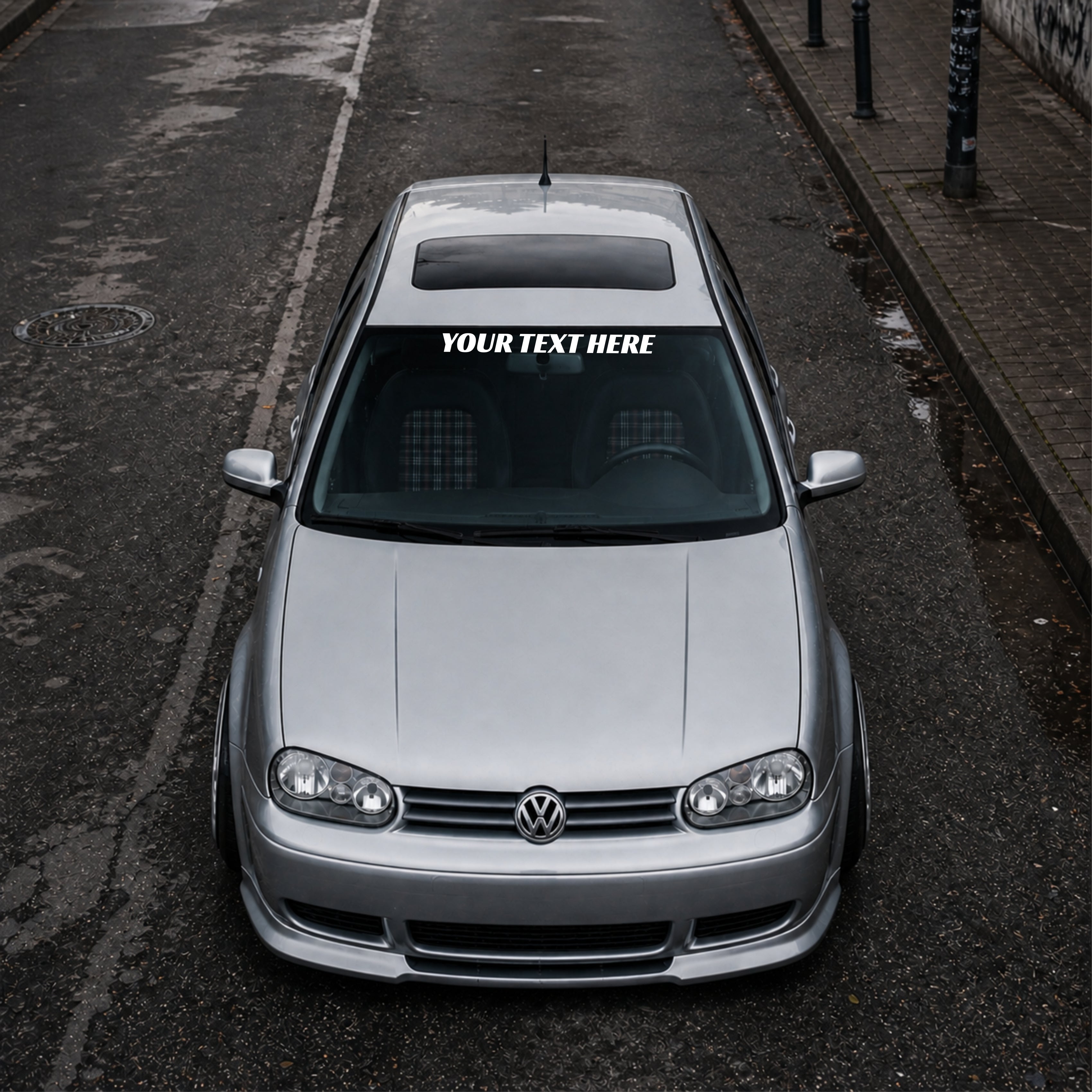 Silver Volkswagen car with a distinctive sticker on the windshield, parked on an urban street.