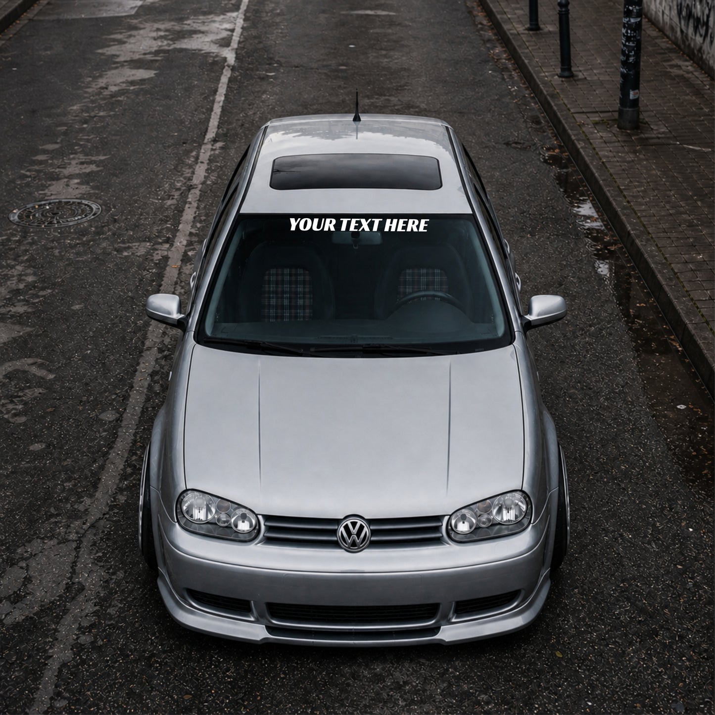 Silver Volkswagen car with a distinctive sticker on the windshield, parked on an urban street.