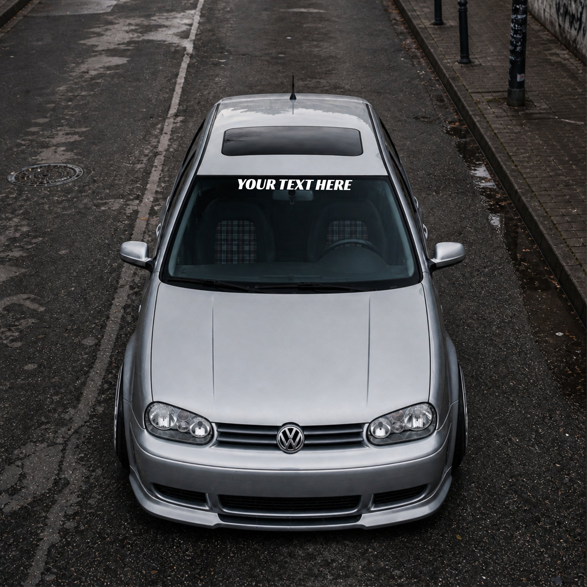 Silver Volkswagen car with a distinctive sticker on the windshield, parked on an urban street.
