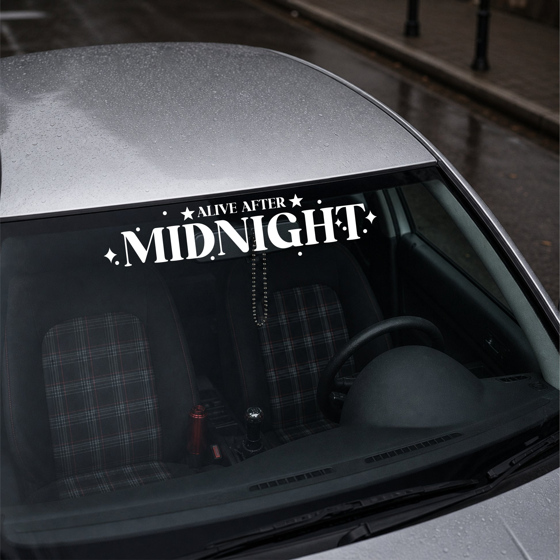 Car window with 'Alive After Midnight' decal on a city street background