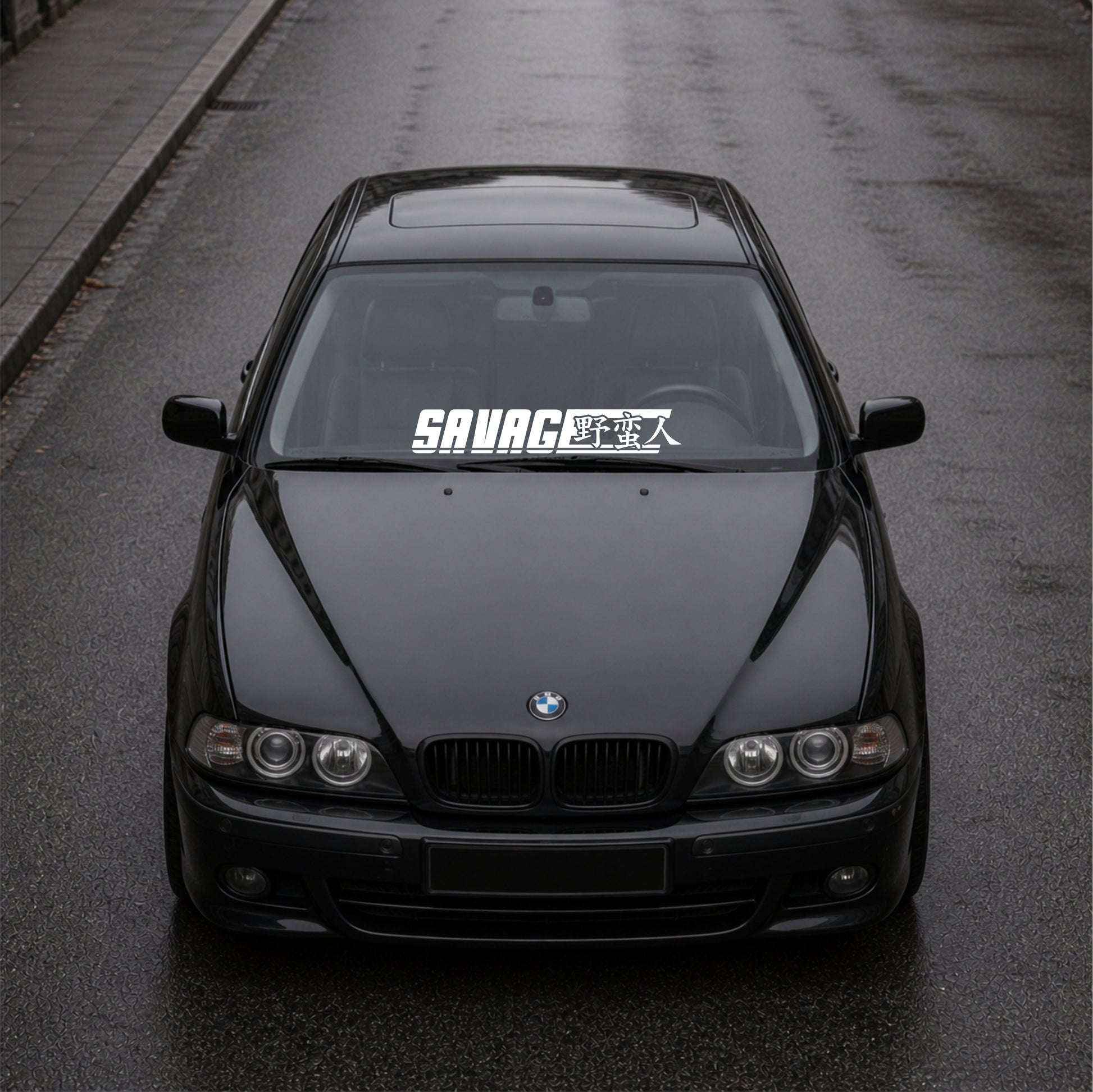 Black BMW car on a road with 'SAVAGE' decal on windshield
