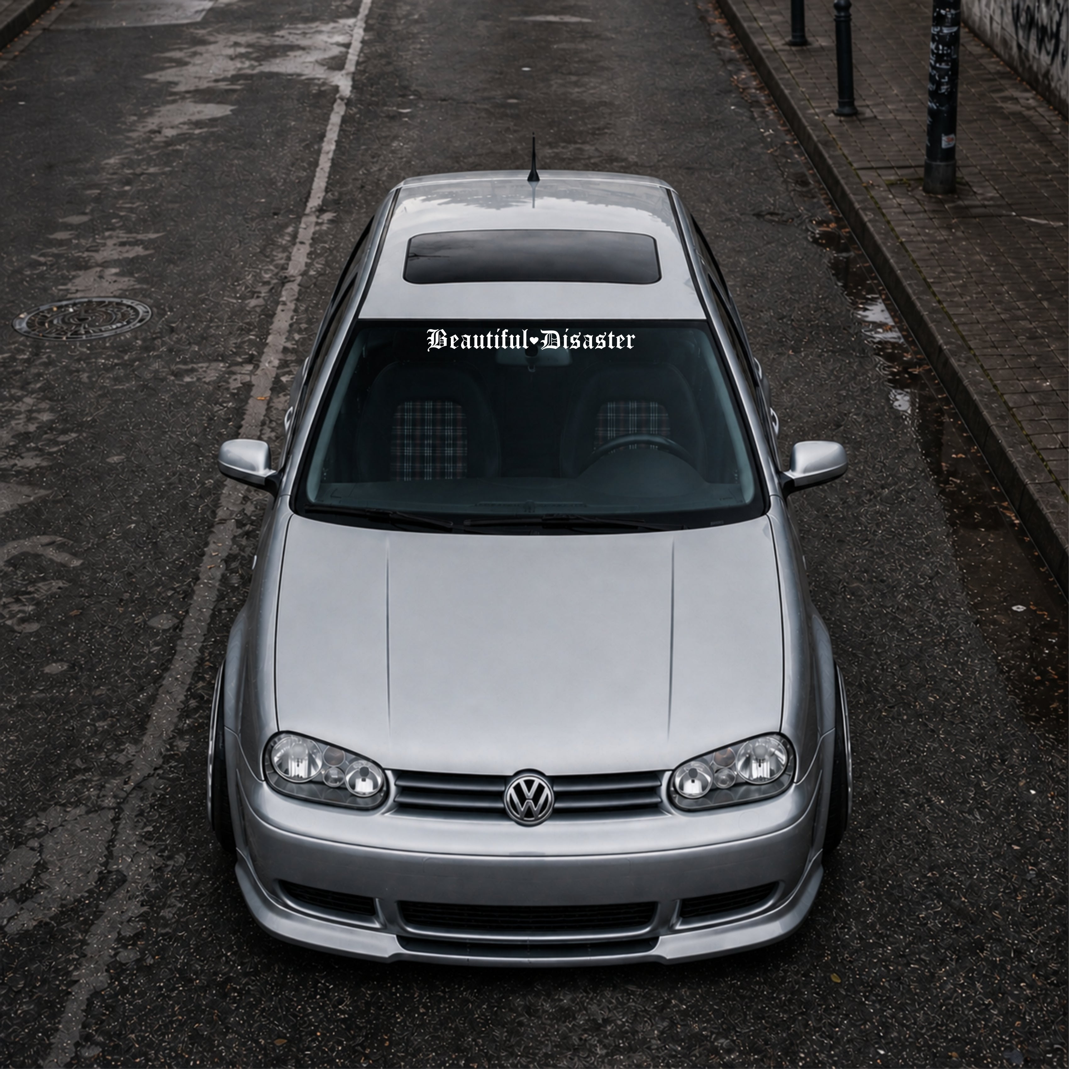 Silver Volkswagen car on a dark street with 'Beautiful Disaster' decal.