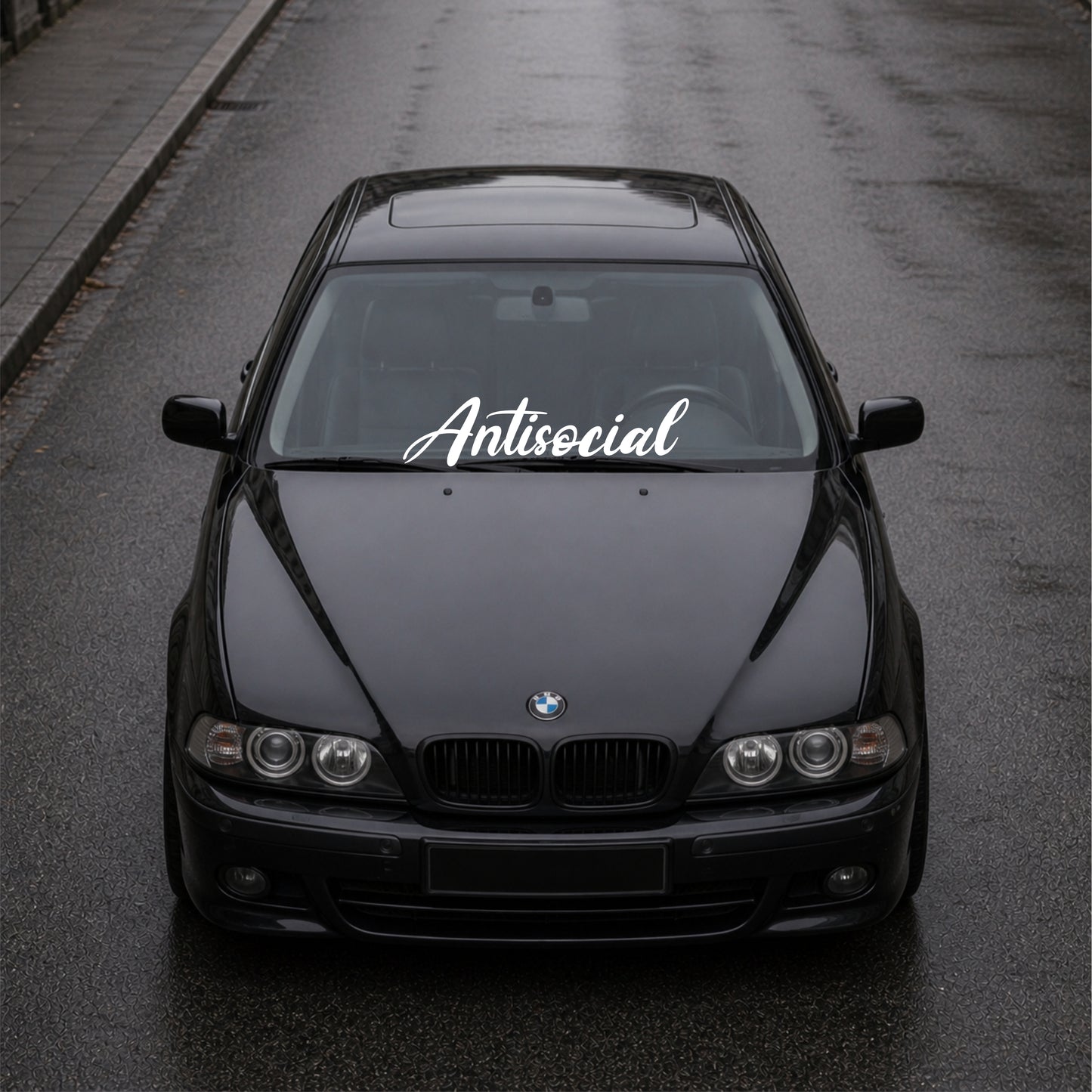 Black BMW car on a road with 'Antisocial' decal on windshield