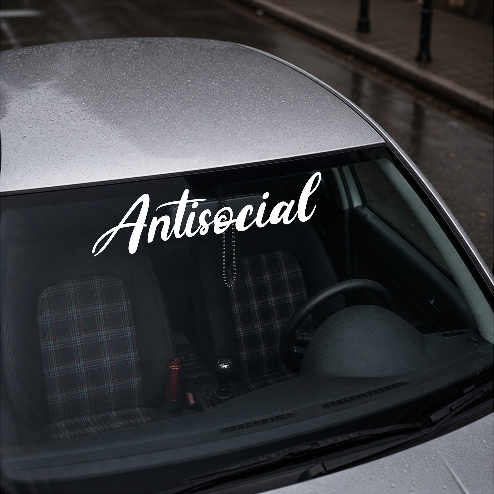 Car window with 'Antisocial' decal on a city street background