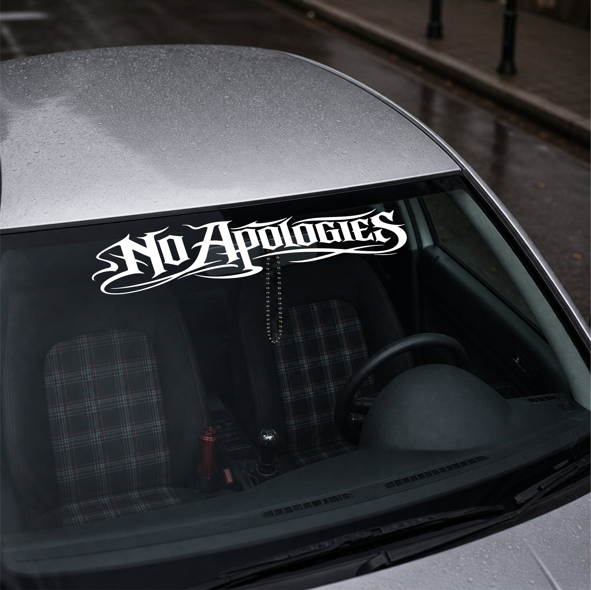 Car window with 'No Apologies' decal on a gray car.