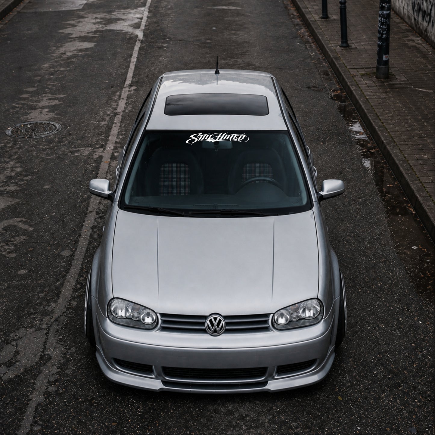 Silver Volkswagen car parked on a street with 'Still hated' branding.