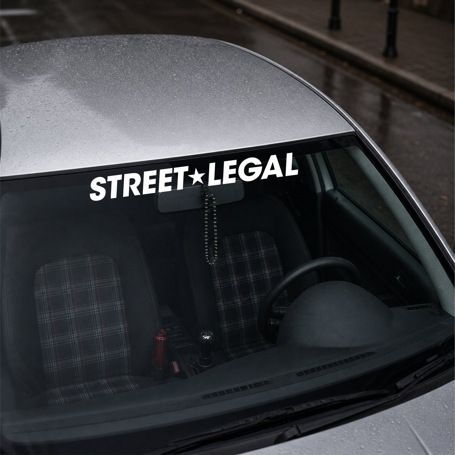 Car window with 'STREET LEGAL' decal on a city street background