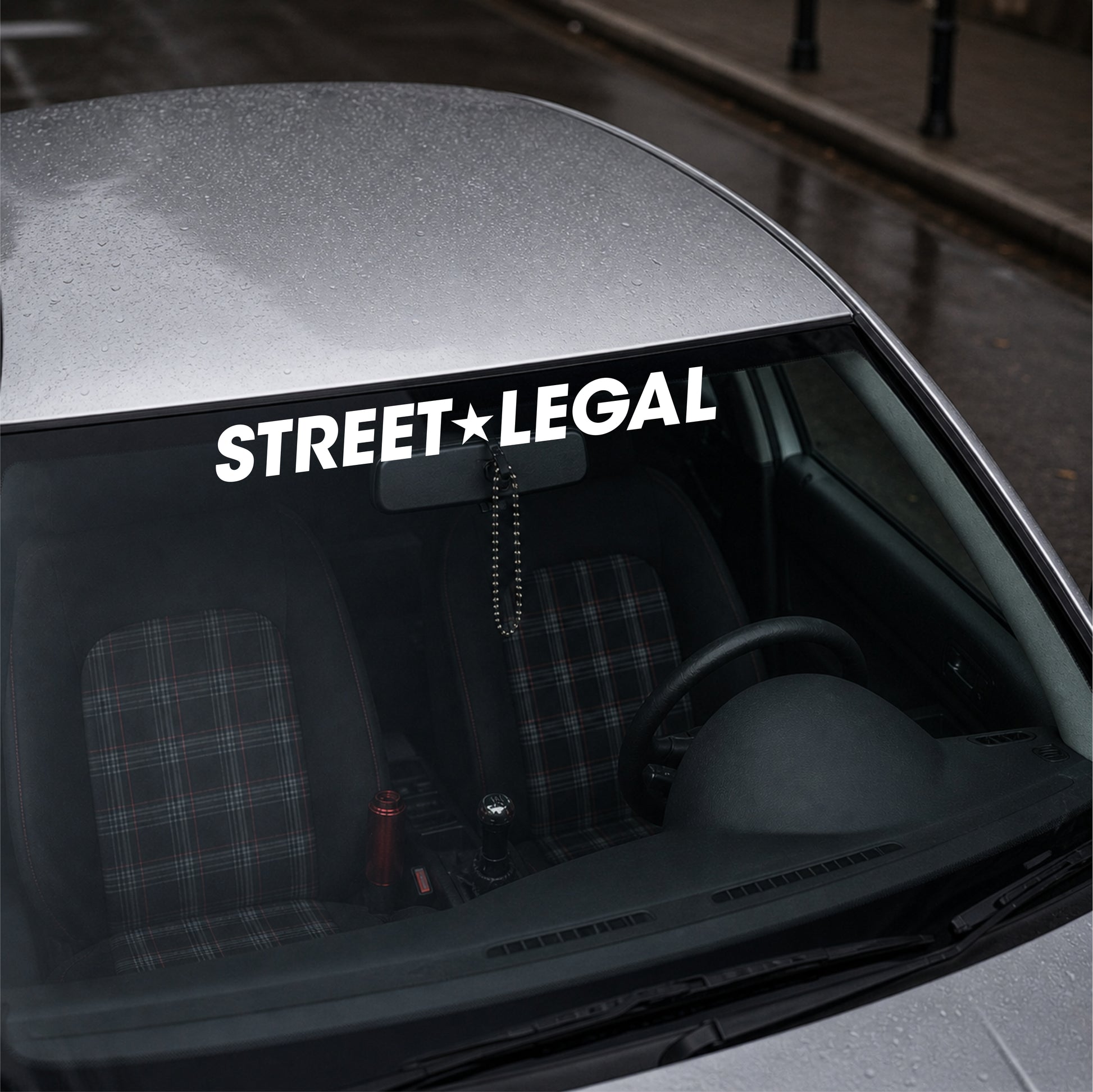 Car window with 'STREET LEGAL' decal on a city street background