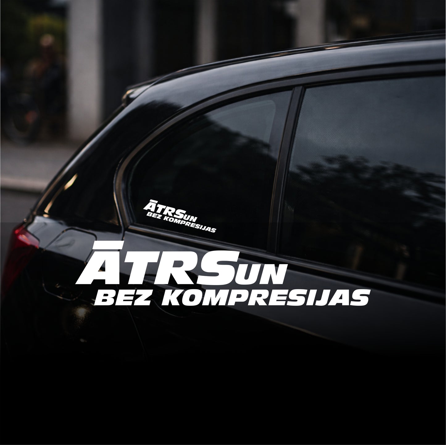Black car with 'ATRSUN BEZ KOMPRESIJAS' decal on a blurred background