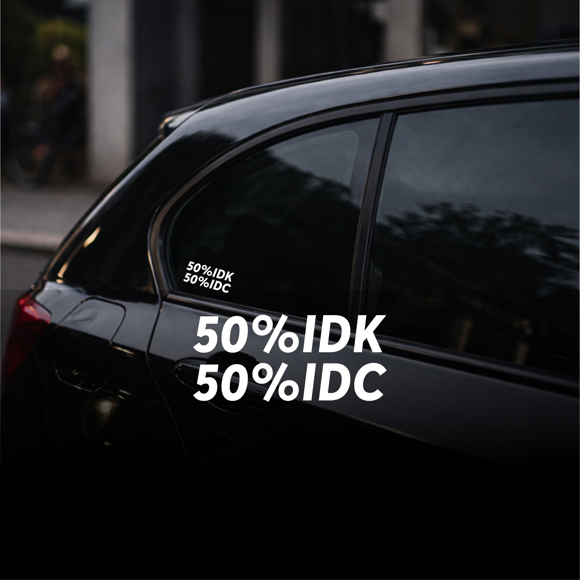 Black car with '50% IDK 50% IDC' decal on a blurred street background
