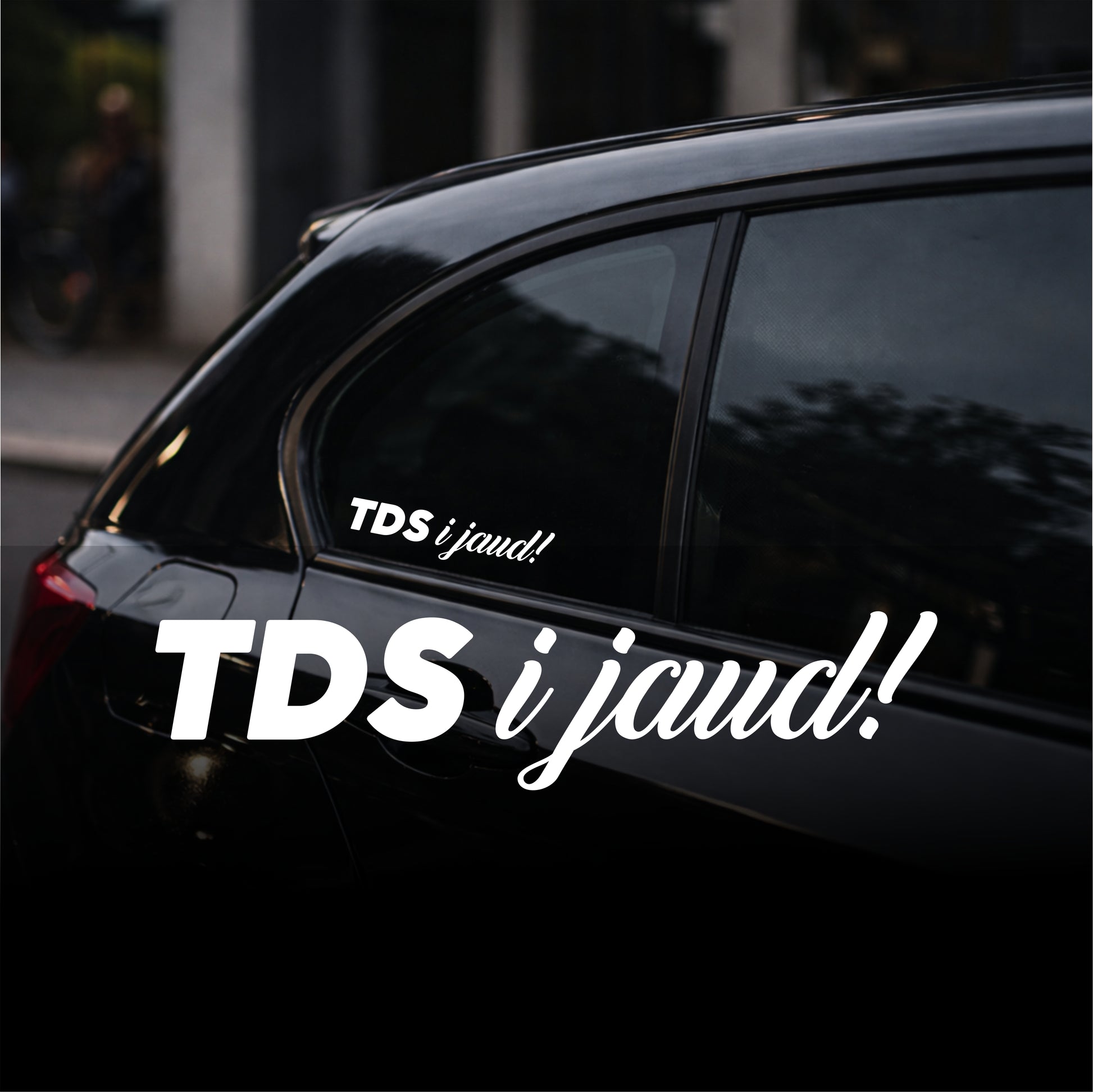 Black car with 'TDS i jaud!' decal on a blurred street background