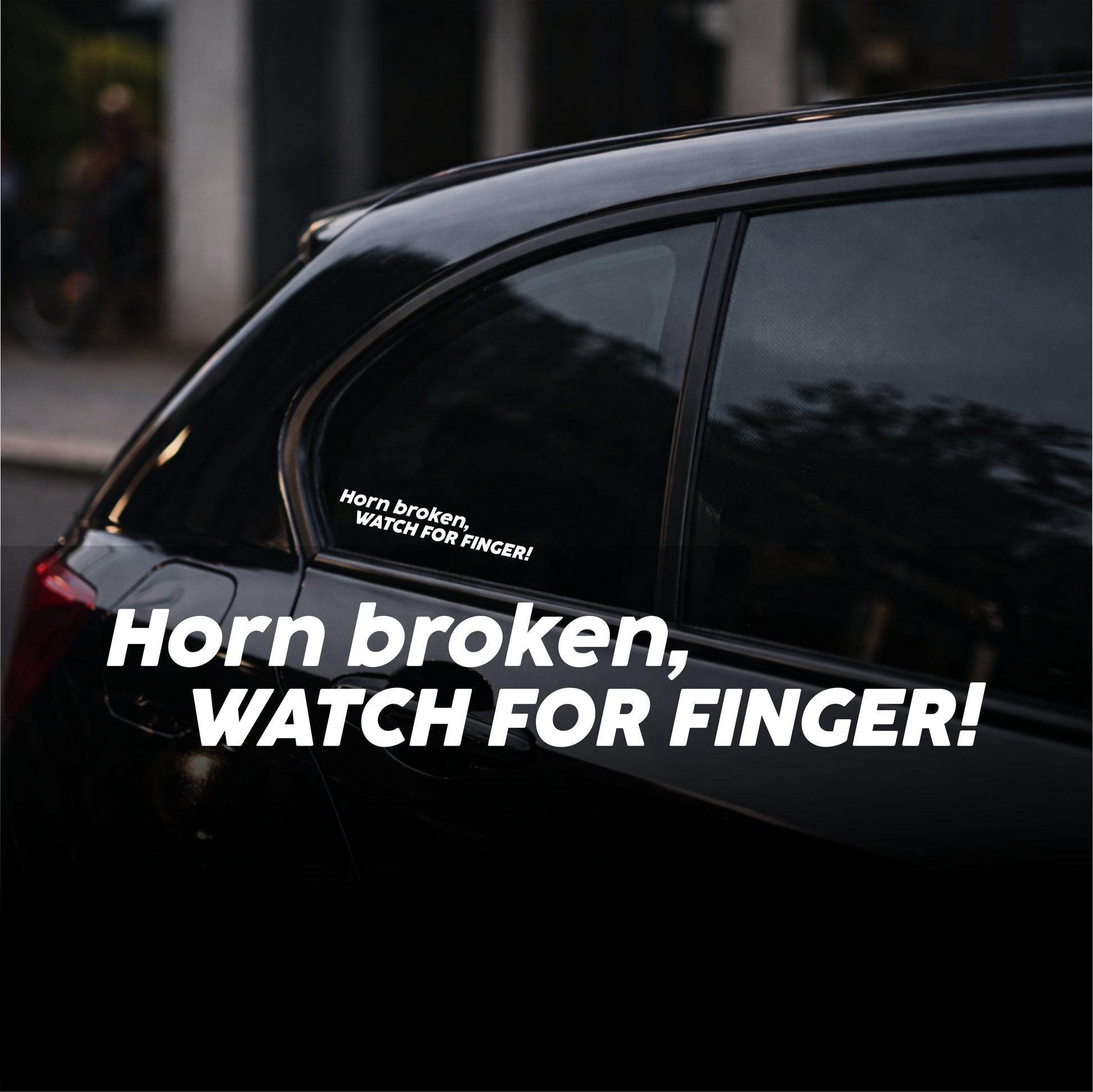Car window with a humorous sticker warning 'Horn broken, watch for finger!' on a dark background.