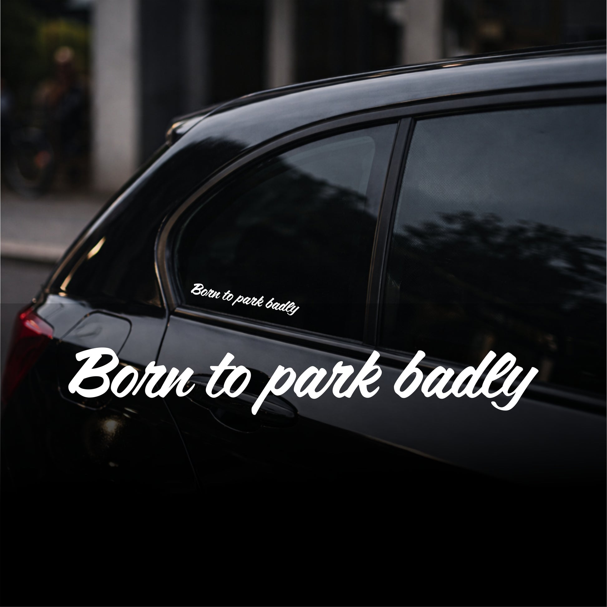 Black car with a humorous 'Born to park badly' sticker on a blurred street background
