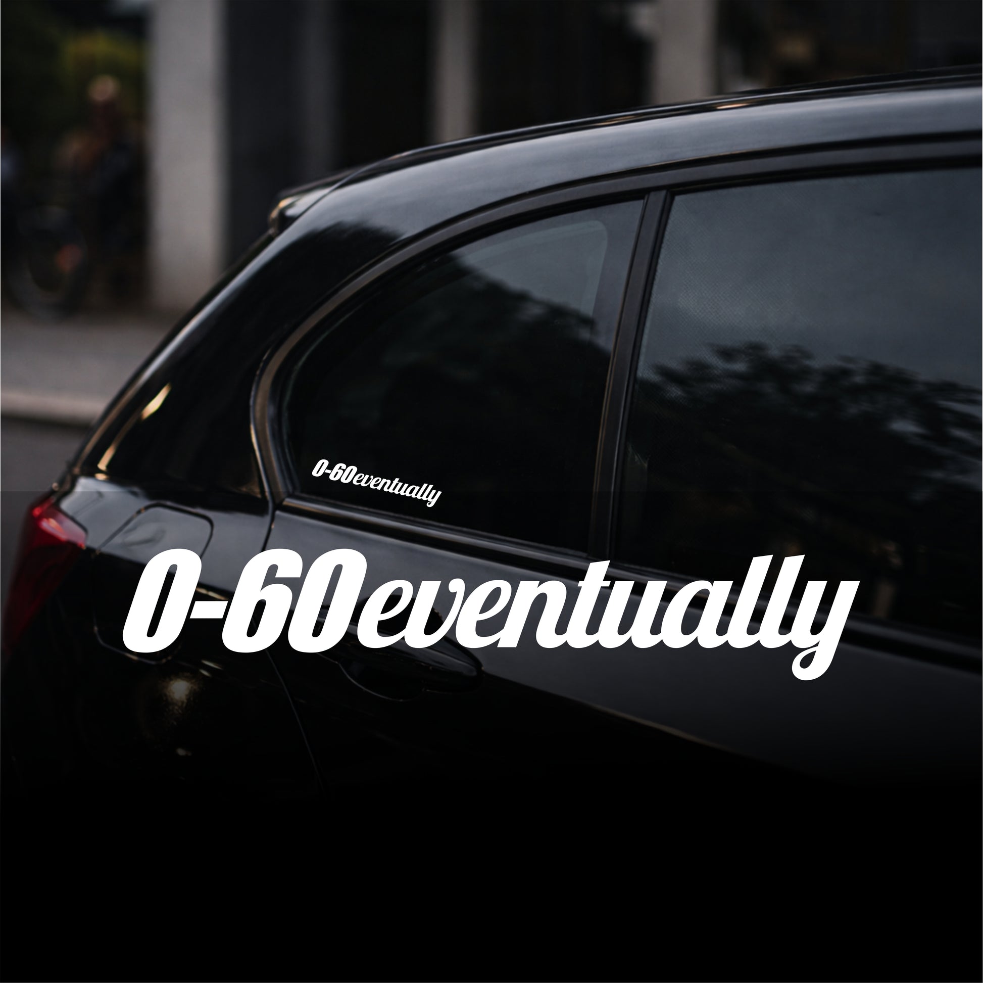 Black car with '0-60eventually' decal on a blurred street background