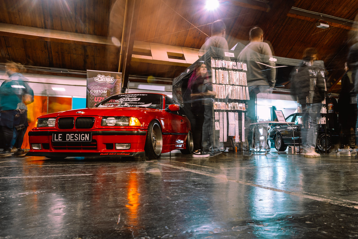 Red car with 'Le Design' on a wooden floor in a garage setting