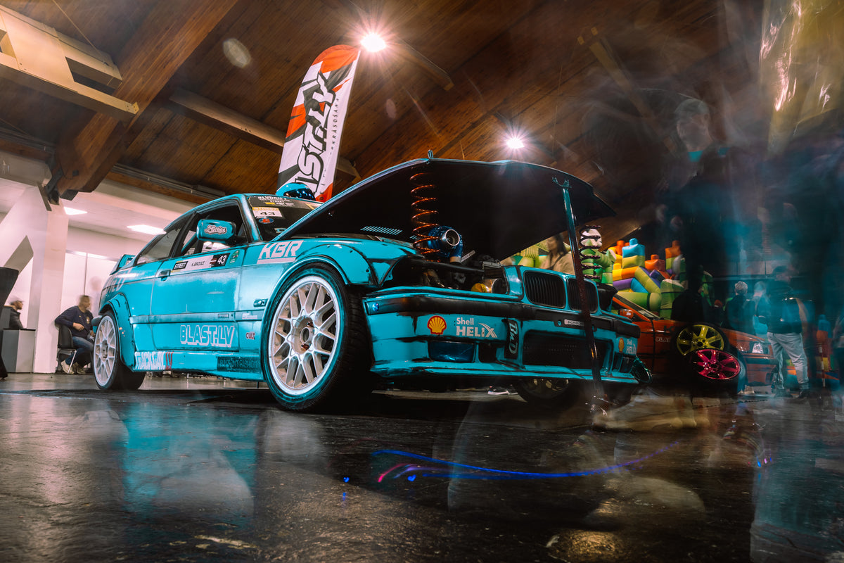 Turquoise car on display in a showroom with a banner in the background