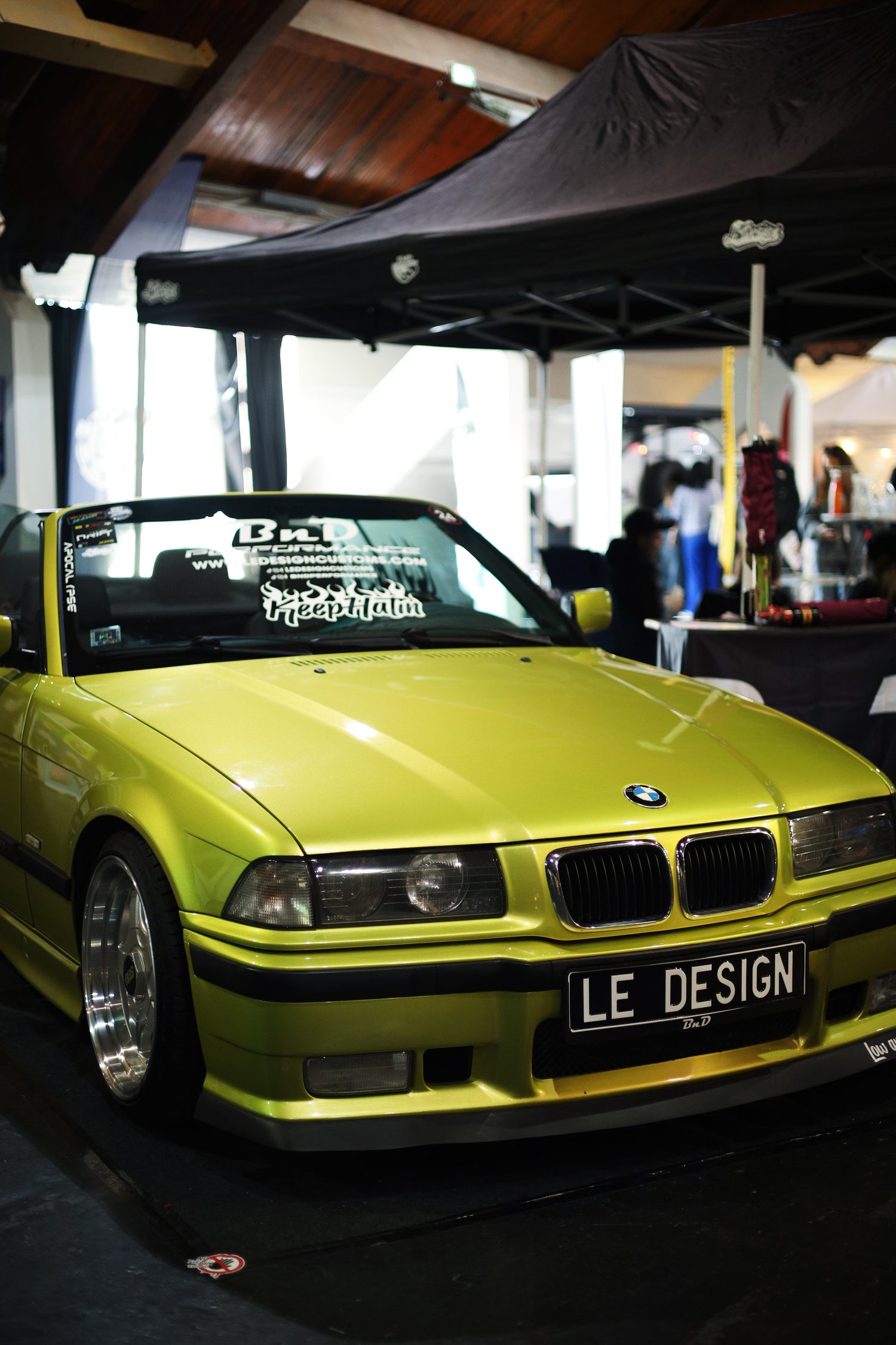 green BMW car with 'LE Design' license plate under a black canopy.
