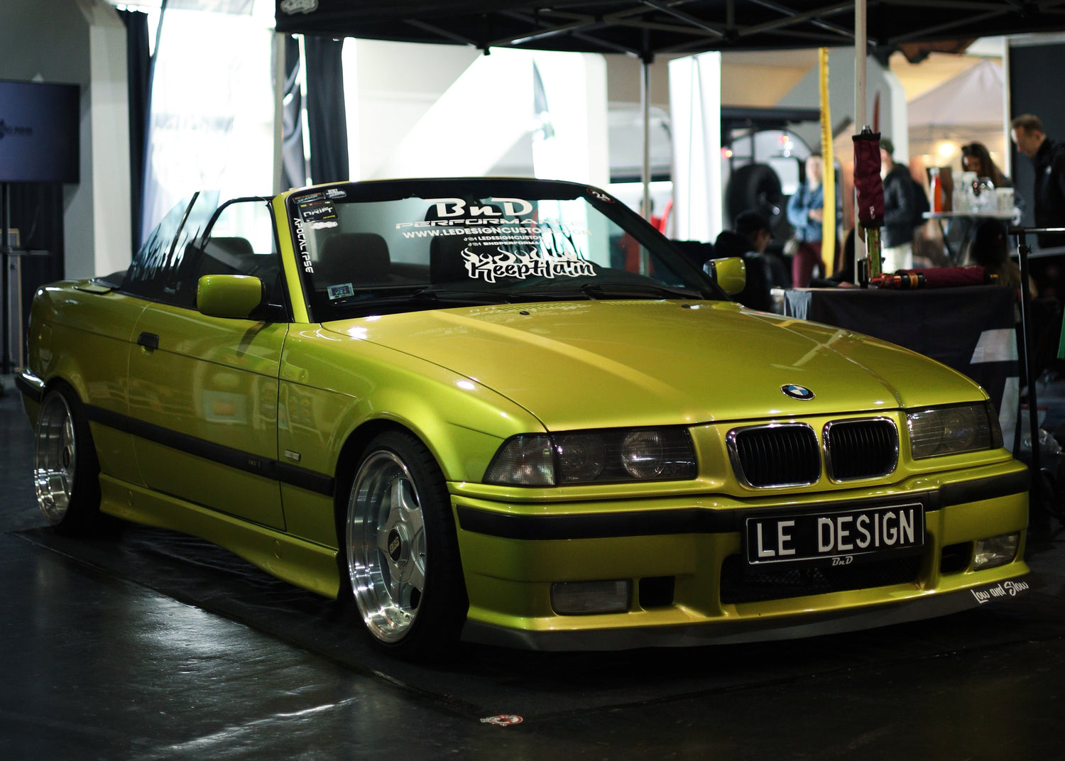 Yellow BMW car on display under a wooden roof structure.