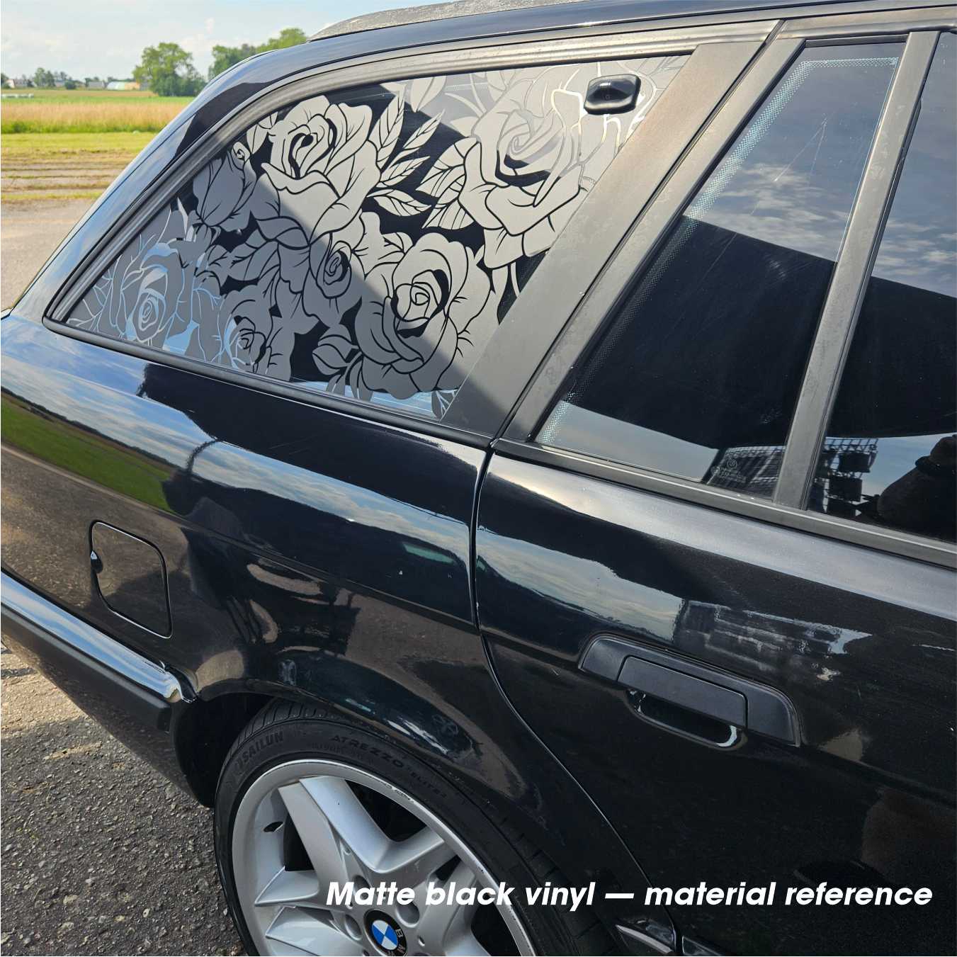 Black car with floral window decal on a rural road