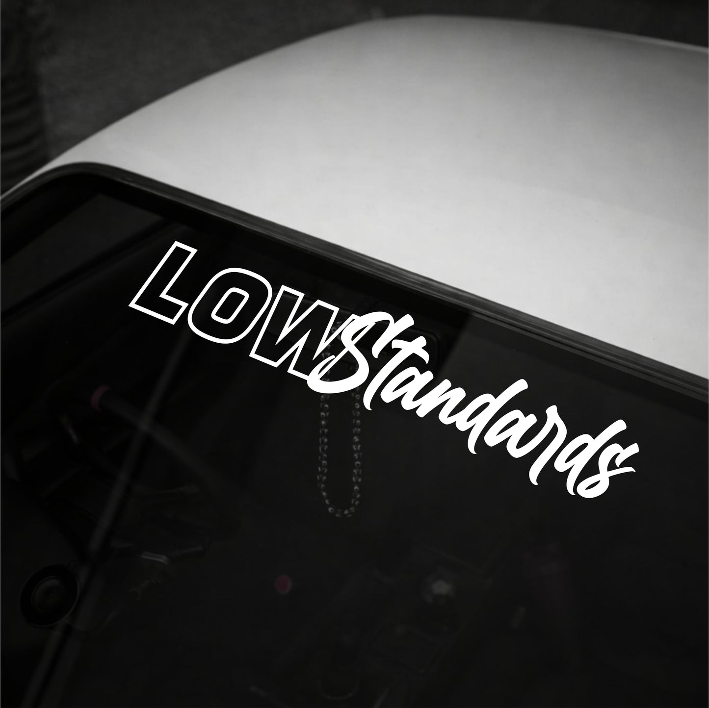Car window with 'Low Standards' decal on a dark background