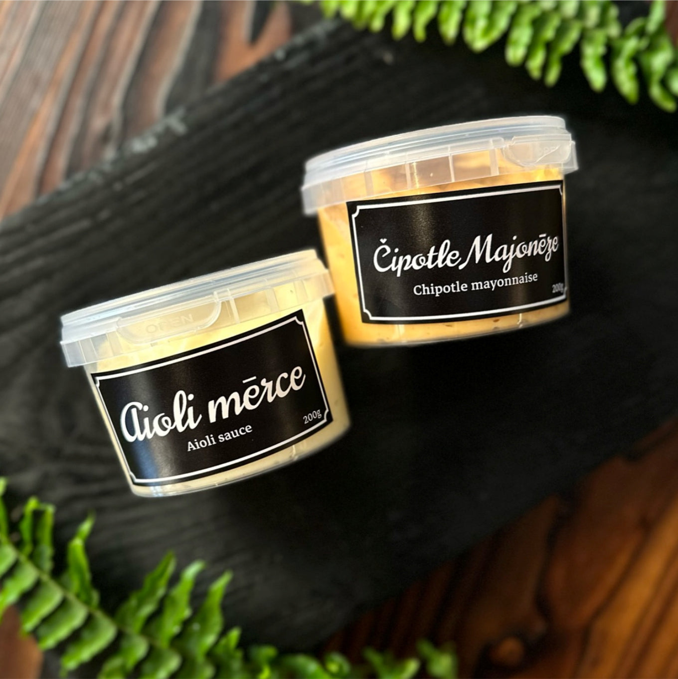 Two containers of aioli sauce with labels on a dark surface.