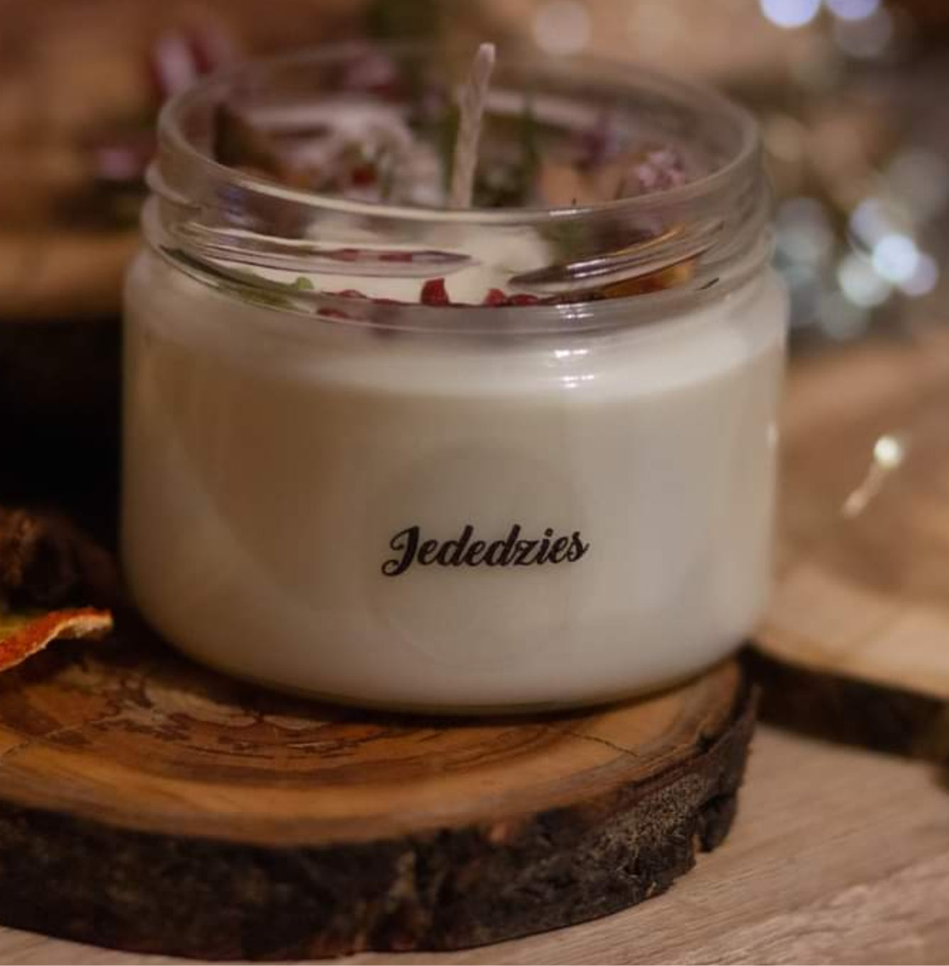 Candle in a glass jar labeled 'Jededzies' on a wooden coaster.